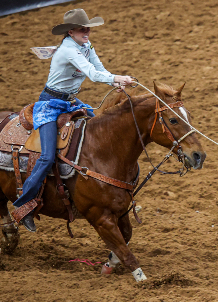 Young female rider competes in rodeo event on chestnut horse in dirt arena.