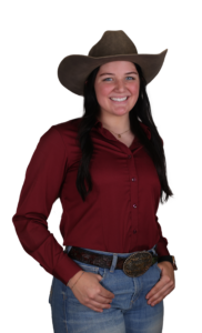 Young woman in modern Western wear: cowboy hat, burgundy shirt, blue jeans with silver belt.