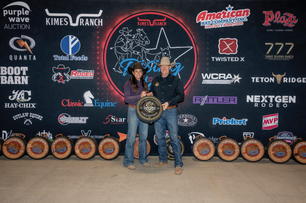 Rodeo champions celebrated with prize buckles at awards ceremony, surrounded by sponsor logos.